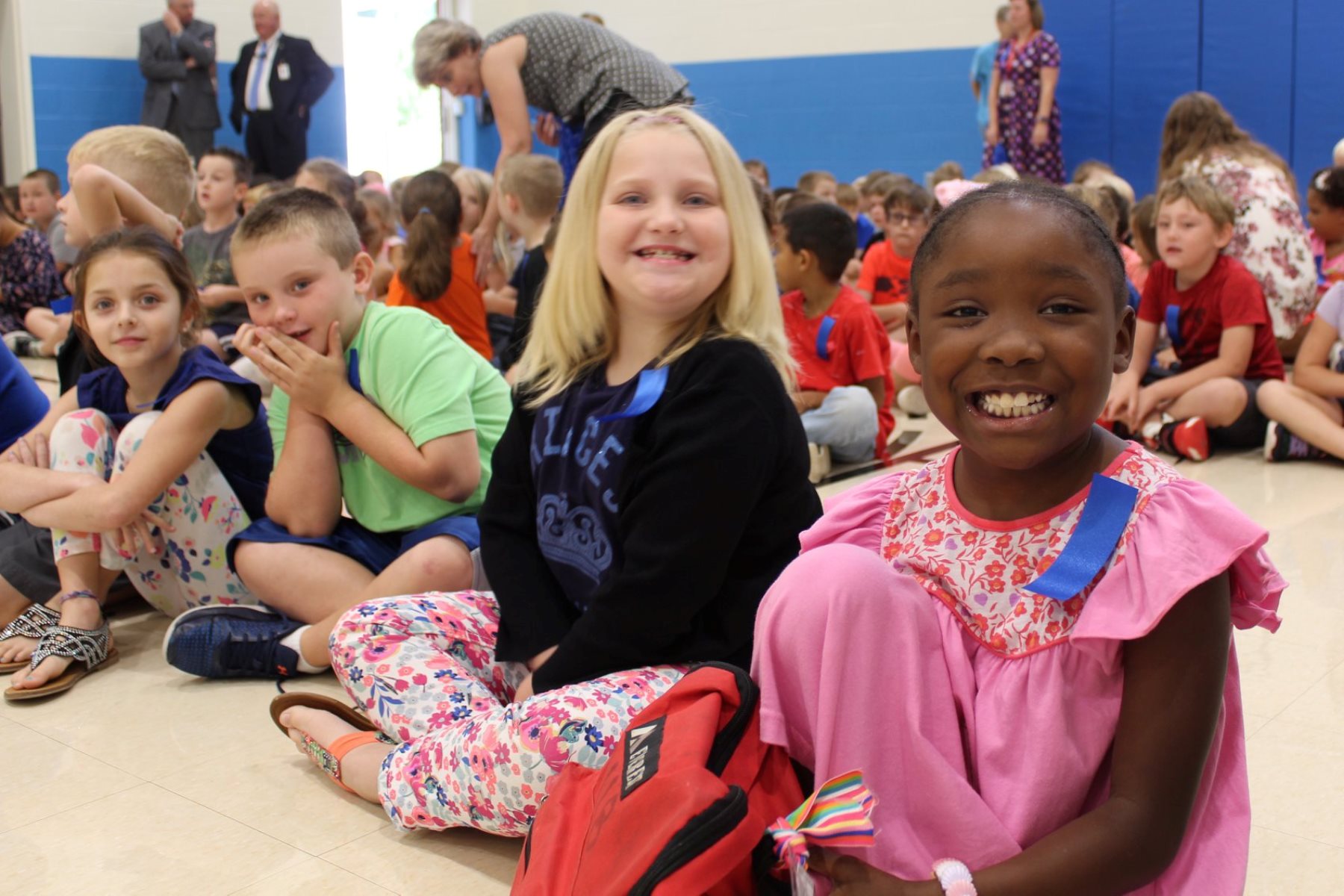 Group of smiling elementary students sitting on the floor of a classroom