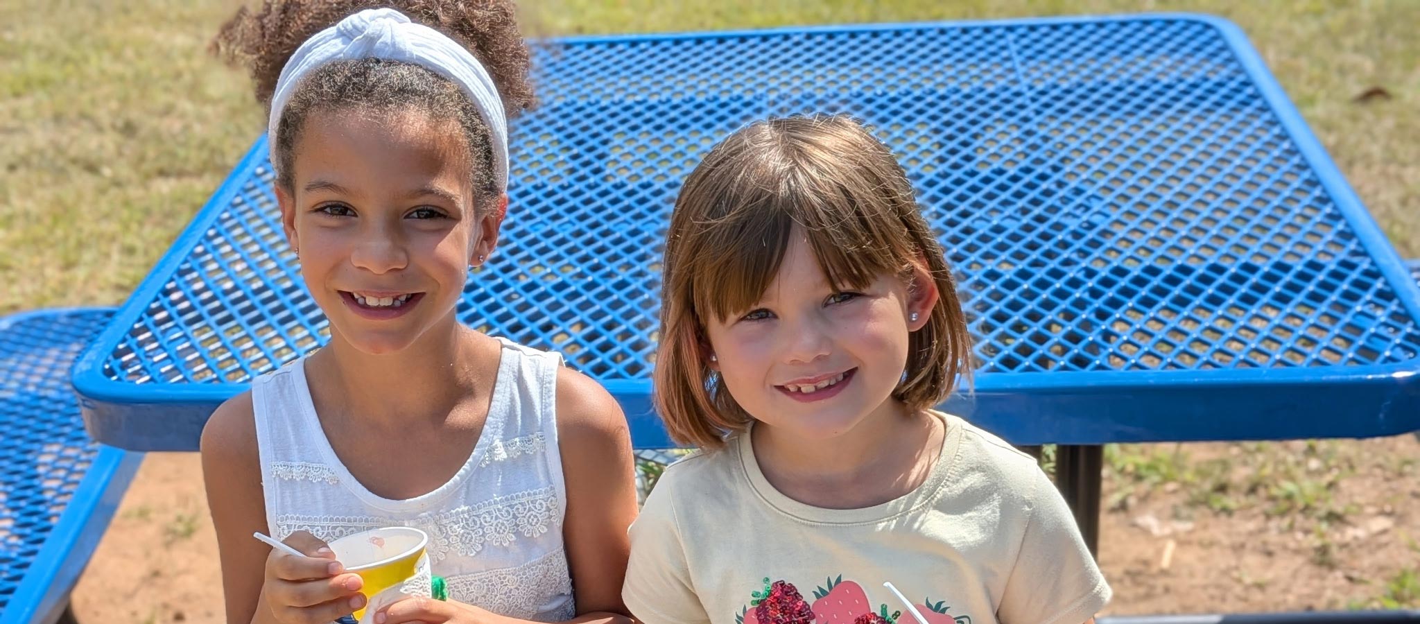 2 smiling girls outside at picnic table
