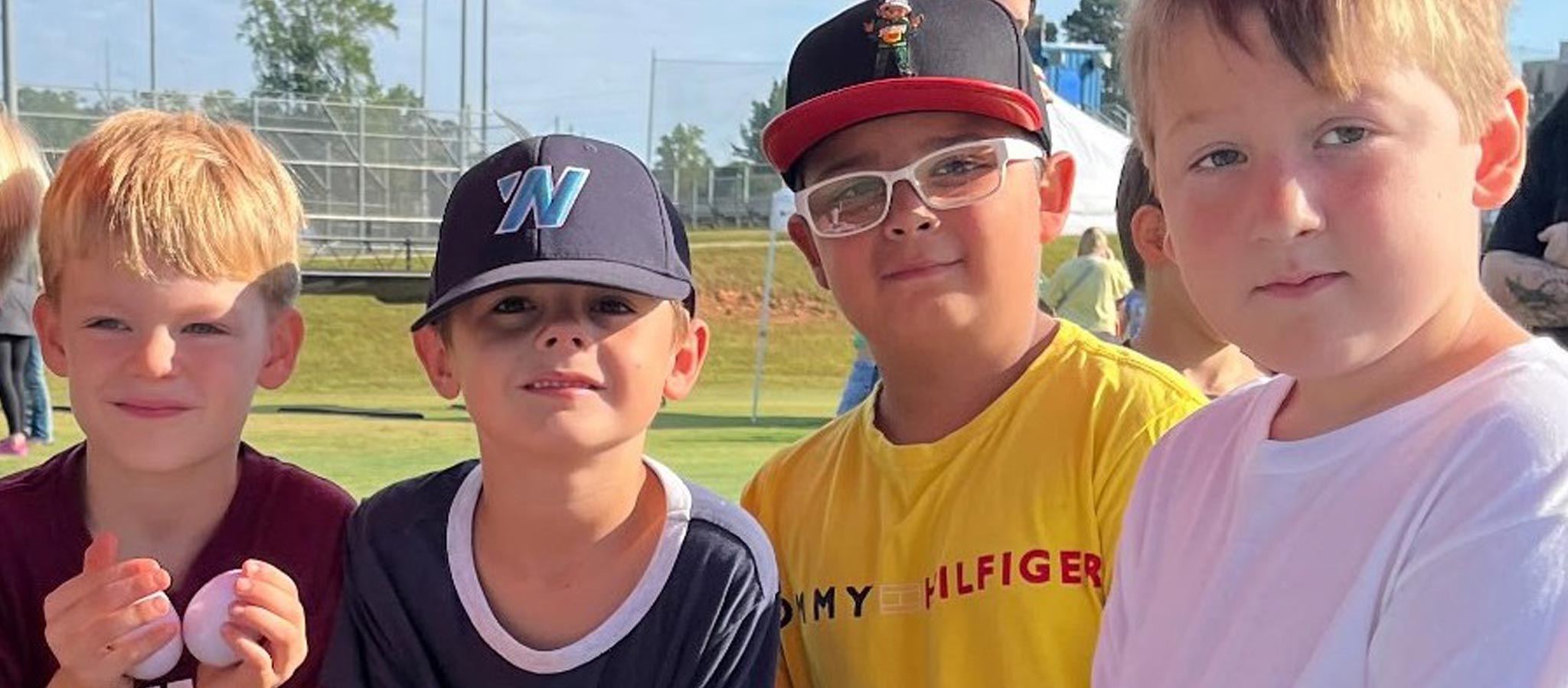 4 boys outside facing camera - 2 with baseball caps