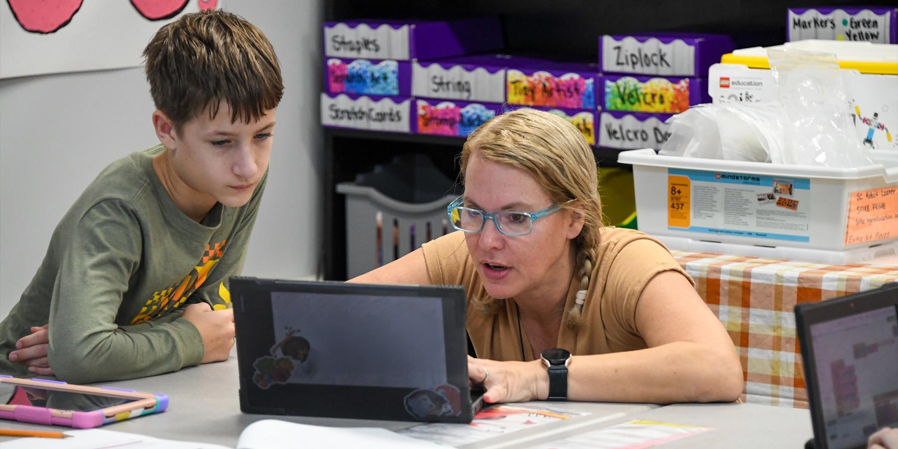 female elementary teacher sharing something with male elementary student on Chromebook