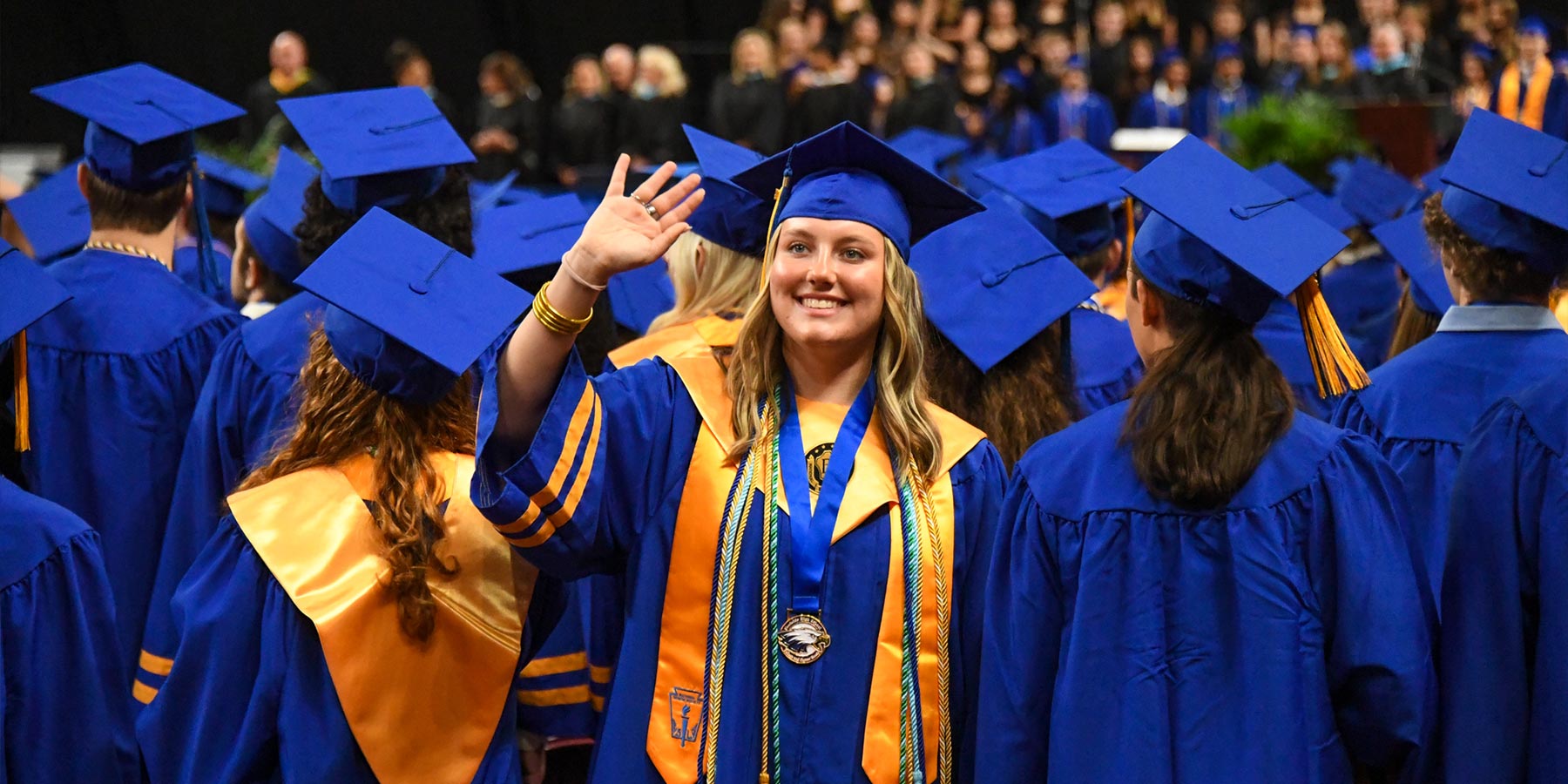 female high school student waving – in graduation regalia