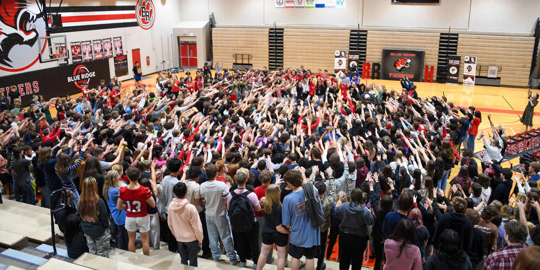 large group of high school students in a gym with hands raised in a pattern