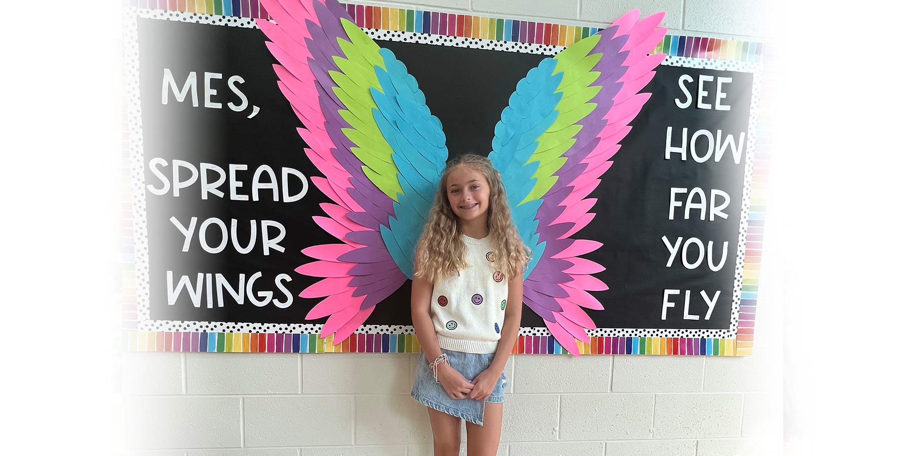 Female student standing in front of an angel-wing bulletin board