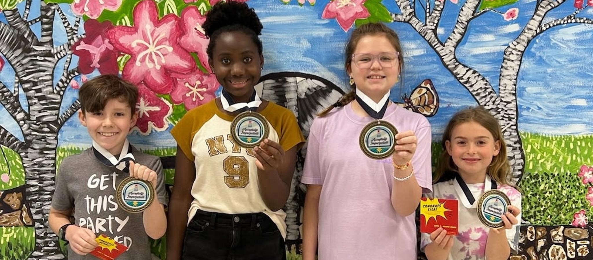 4 Students holding award medals in front of school wall mural