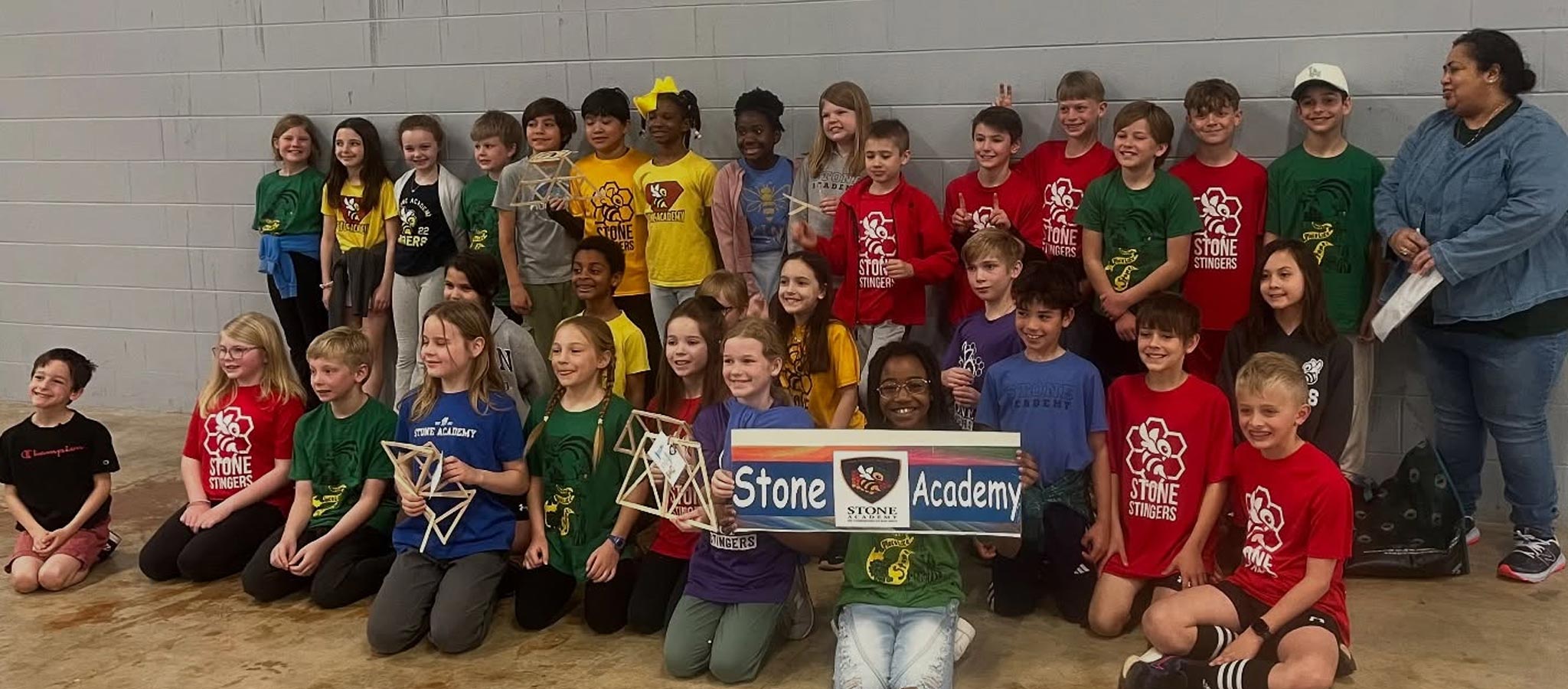 Large group of students posing; some with wooden design structures